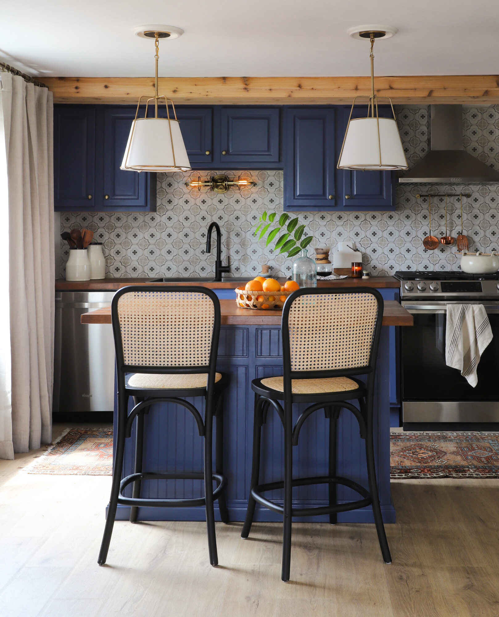 Photograph of newly renovated kitchen with rich, blue cabinets, patterned tile backsplash, gold pendant lights and cane bar stools.