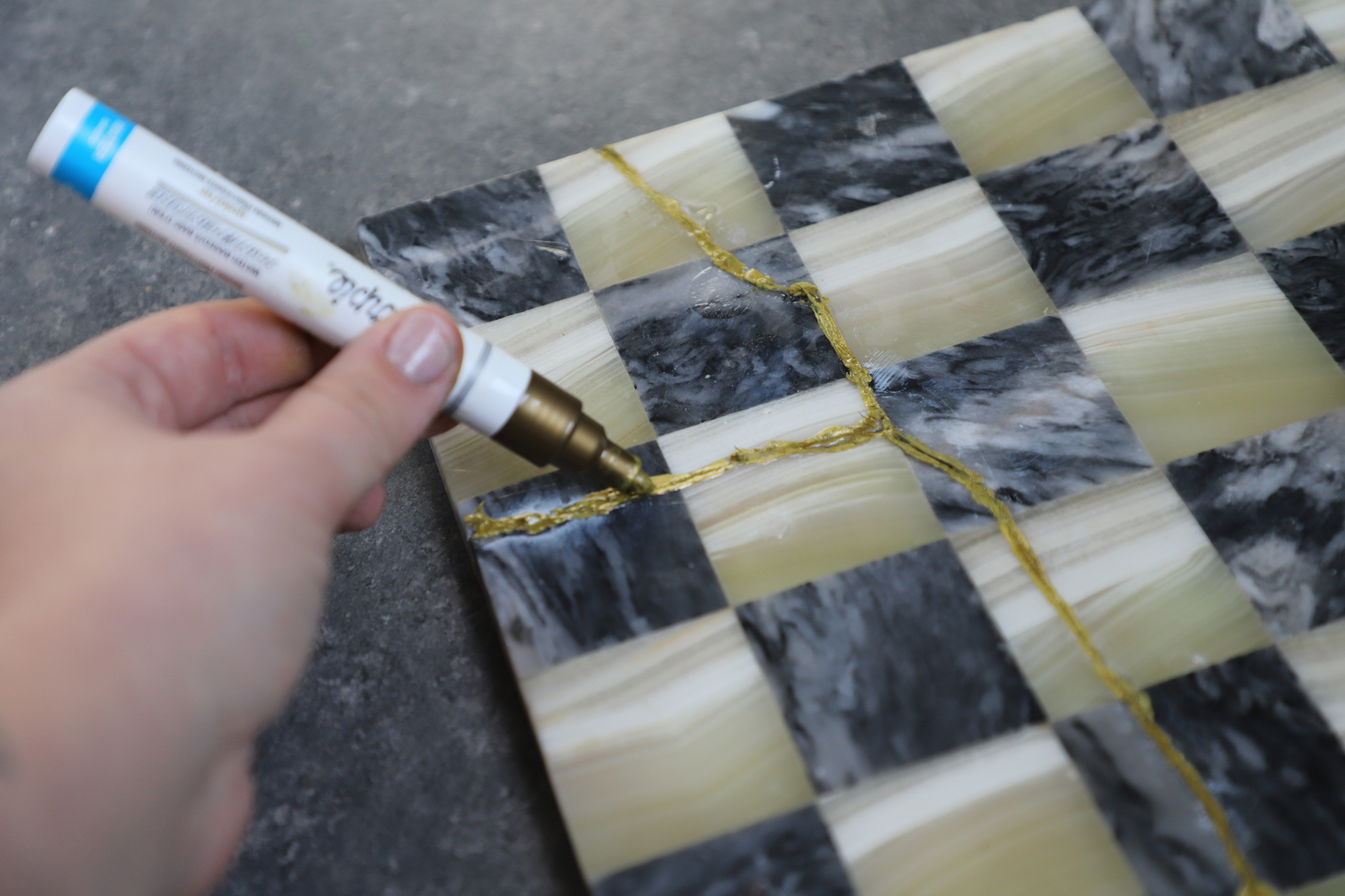 Using gold paint pen to add detail to glued chess board.