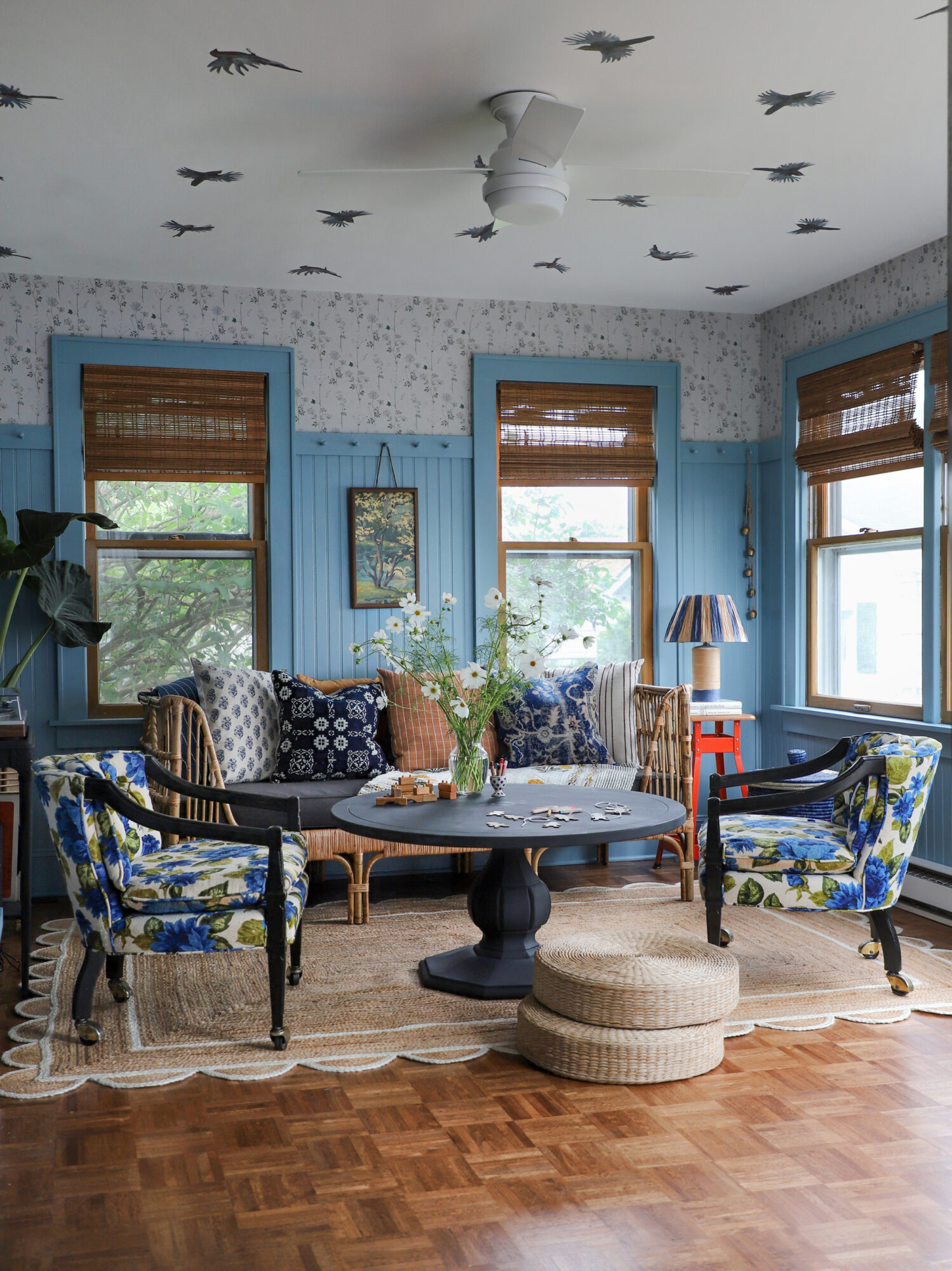Beautiful sunroom with eclectic thrifted furniture, blue board and batten details and seating for the whole family.